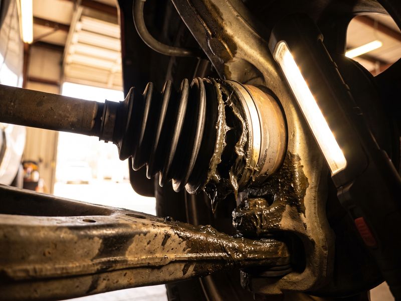 A split black CV axle boot under the car with grease sprayed across the inside of the wheel well